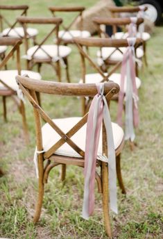 rows of wooden chairs with pink ribbons tied to them in the grass at an outdoor ceremony