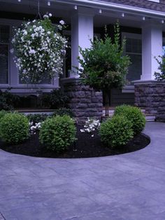 a house with white flowers in the front yard and bushes on the side of the house