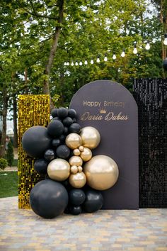 black and gold balloons are placed in front of a sign that reads happy birthday debra