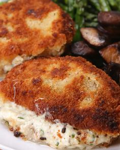 two crab cakes on a white plate with mushrooms and broccoli in the background