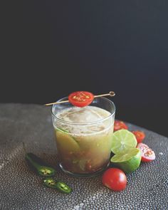 a glass filled with liquid next to tomatoes and limes