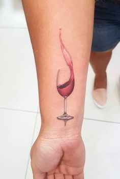 a woman's arm with a wine glass tattoo on the left side of her wrist