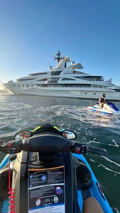 two people on jet skis in the water near a large white boat and yacht