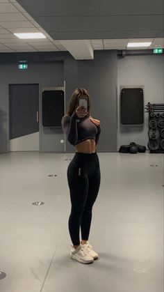 a woman taking a selfie with her cell phone in an empty gym room filled with exercise equipment