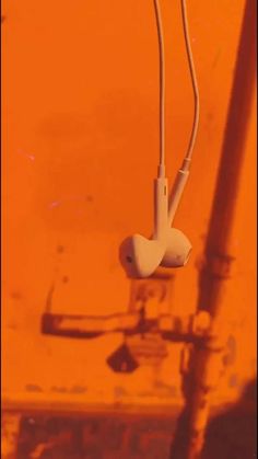 earphones hanging from wires in front of an orange wall with the reflection of another device on it