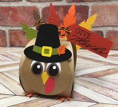 a paper turkey with a pilgrim hat and leaves on it's head, sitting in front of a brick wall