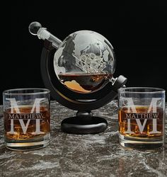 two glasses and a decanter are sitting on a marble counter top with a globe in the middle