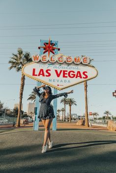 a woman standing in front of the welcome to las vegas sign with her arms outstretched