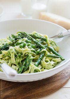 a white bowl filled with pasta and asparagus on top of a wooden cutting board