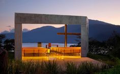 an outdoor area with benches and a cross in the center at dusk, near water