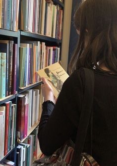 a woman is reading a book in front of a bookshelf full of books