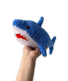 a hand is holding a knitted toy that looks like a shark