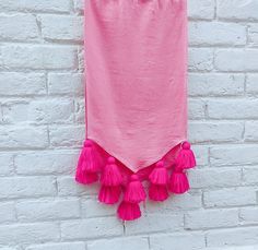 a pink towel hanging on a white brick wall with tassels in front of it