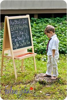 a young boy standing in front of a chalkboard with writing on it and an easel next to him