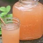 two jars filled with liquid sitting on top of a wooden table next to green plants