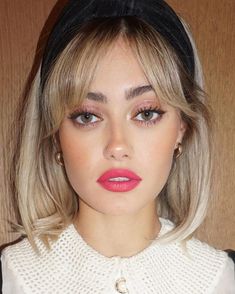 a woman with blonde hair wearing a black and white sweater, pink lipstick and gold earrings