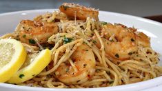 a white bowl filled with pasta and shrimp on top of a table next to a lemon wedge