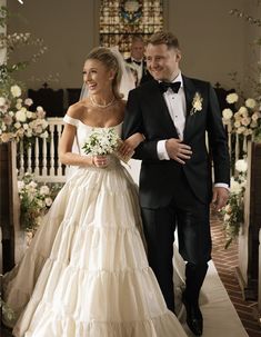 the bride and groom are walking down the aisle in their wedding gowns, which is adorned with white flowers