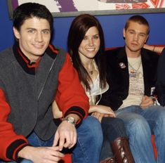 four people sitting on a red couch in front of a blue wall with an american flag