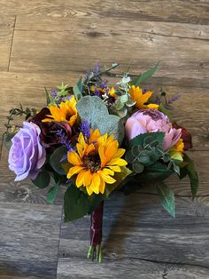 a bouquet of sunflowers, roses and other flowers sits on a wooden surface