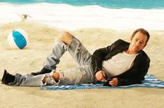 a man laying on top of a beach next to a blue and white ball