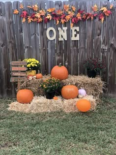 pumpkins and hay bales in front of a one sign on a wooden fence