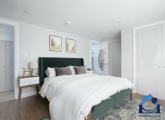 a bedroom with white walls and wood flooring has a green headboard on the bed