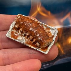 a hand holding a piece of tin foil with some food on it and fire in the background