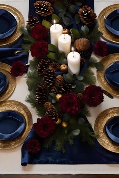 the table is set with candles, pine cones and red flowers on blue napkins