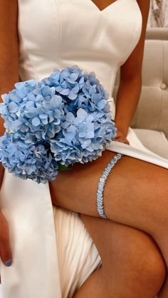 a woman in white dress holding a bouquet of blue hydrangeas on her knee