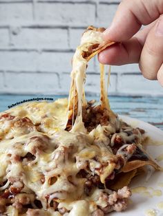 a person is dipping cheese on top of nachos with ground beef and melted cheese