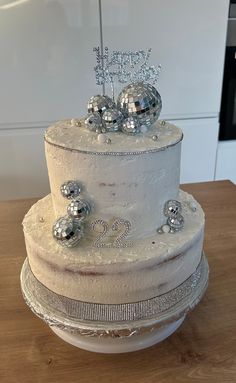 a three tiered white cake with silver decorations on the top and bottom, sitting on a wooden table