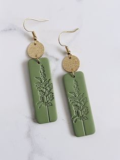 two green and gold earrings with flowers on them sitting on a marble counter top next to each other