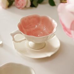 a pink tea cup sitting on top of a white saucer next to some flowers