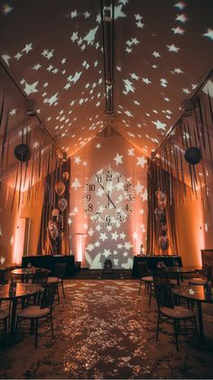 Dimly lit event room with star-shaped lights projected on the ceiling, tables arranged around a large wall clock, and festive decorations.