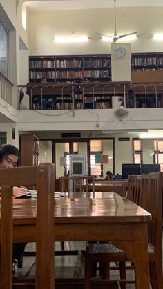 a woman sitting at a wooden table in front of a book shelf filled with books