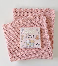 a pink crocheted blanket with an abc love sticker on the front and bottom