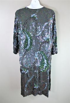 "This dress is of a black silk with iridescent sequins and beading in abstract patterns. The green is a paisly shape but also resemble a leaf. there are channels or pearl beads alsolots to look at! It is in excellent vintage conditon and is marked size M, but we feel it is larger. The first pic is on a larger dress form and the third pic is on a size 4 dress form (just to give reference). Estimated L/XL Marked M 48\" total bust 48\" waist 50\" hip 18\" shoulder to shoulder Purveyor's Note: We ha Green Embellished Sequin Dress For Formal Occasions, Green Embellished Sequin Dress For Evening, Evening Silk Dress With Sequins, Embellished Silk Sequin Evening Dress, Silk Cocktail Dress With Sequins, Silk Sequin Cocktail Dress, Glamorous Silk Dress With Sequins, Fitted Silk Sequin Dress, Silk Sequin Dresses For Party Season