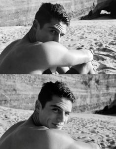 a man sitting on top of a sandy beach next to the ocean with his shirt off