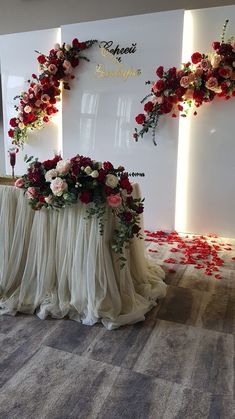 an arrangement of flowers and petals on display in front of a white backdrop with red roses