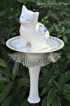 a white cat statue sitting on top of a bird bath