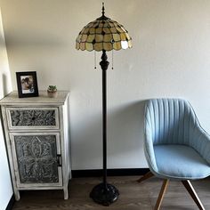 a blue chair sitting next to a lamp on top of a wooden floor in front of a white wall