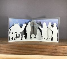 an open card with cut out silhouettes of people standing in front of a nativity scene