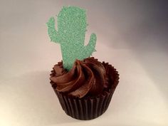 a cupcake with chocolate frosting and a green cactus topper sitting on a white surface