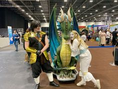 two women standing next to a statue of a dragon and a woman in white dress