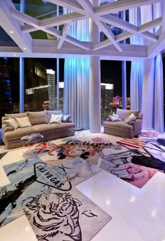 a living room filled with lots of furniture and art work on the floor in front of large windows