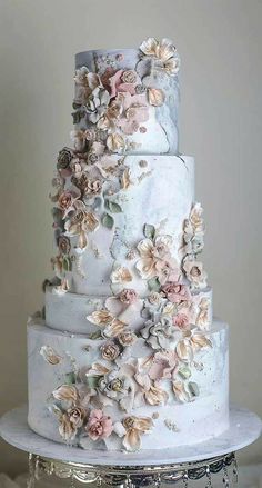 a three tiered wedding cake with flowers on the top and bottom, sitting on a silver platter