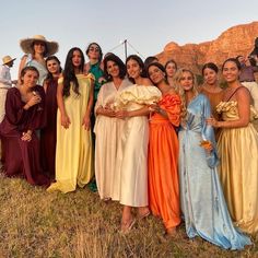 a group of women standing next to each other in long gowns and holding flowers