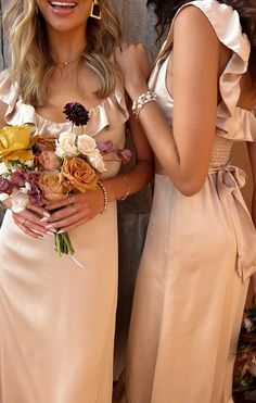 two beautiful women standing next to each other holding bouquets in their hands and smiling at the camera