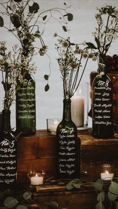 three bottles with flowers in them sitting on top of a wooden table next to candles